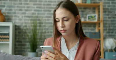 Mulher lendo uma mensagem no celular em casa, sentada no sofá